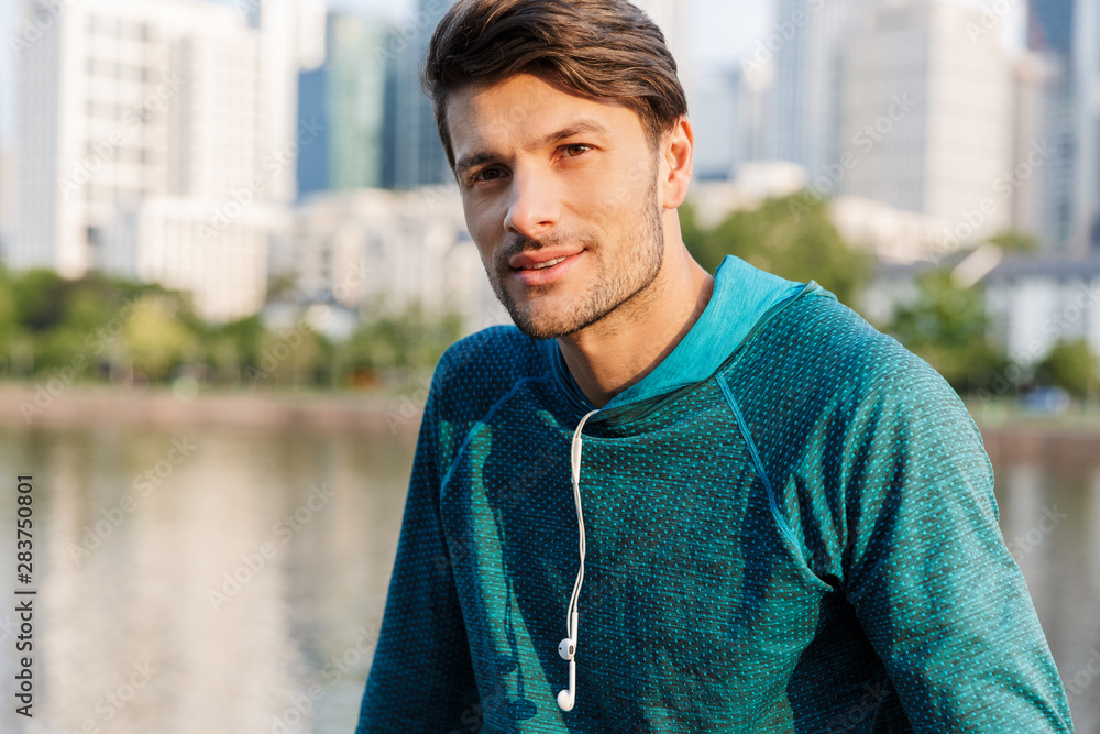 Photo closeup of satisfied young man looking at camera while working out near city promenade Photo closeup of satisfied young man looking at camera while working out near city promenade