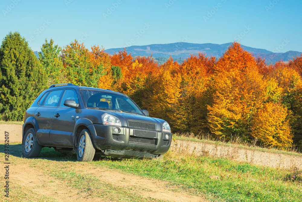 suv on the gravel country road side in mountains. trees in colorful fall foliage on the background. ridge in the distance. travel by car concept