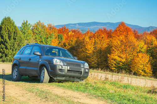 suv on the gravel country road side in mountains. trees in colorful fall foliage on the background. ridge in the distance. travel by car concept