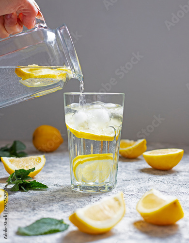 Water with lemon, mint and ice. Water is poured from a glass jug into a glass. Close-up.