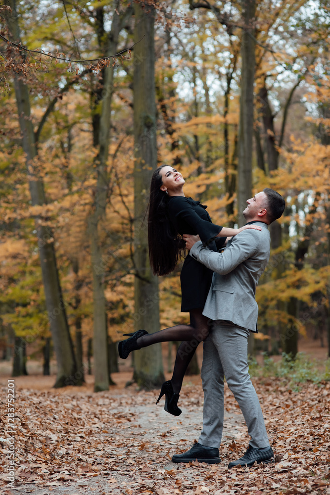 Fototapeta premium Happy young couple in love. The guy holding his girlfriend in his arms. Romantic relationship in autumn forest. Love story. To love each other.