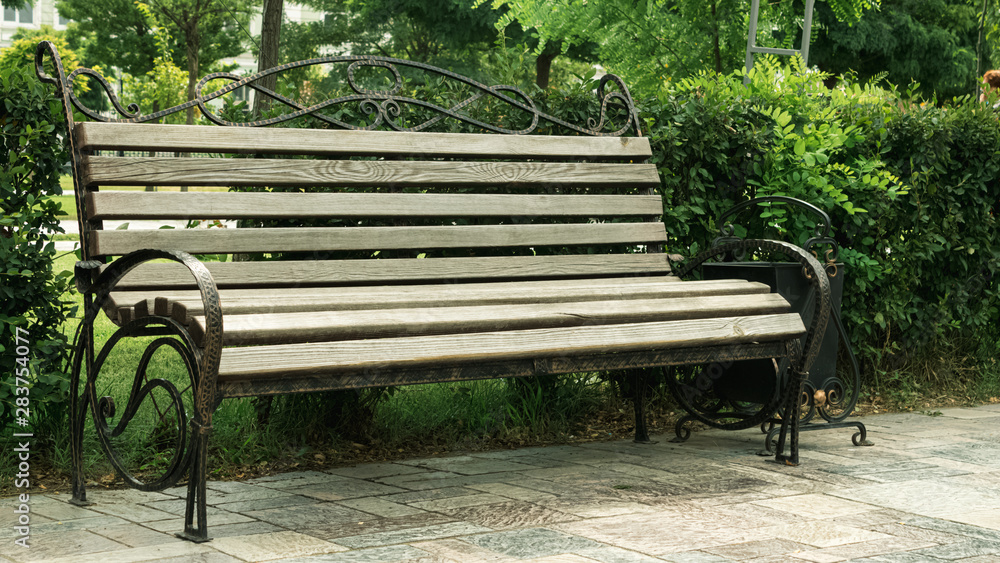 Wooden bench with metal art forging in the amusement park. Brown bench on the green background of nature. Wooden bench with metal art forging in the amusement park. Brown bench on the green background of nature.