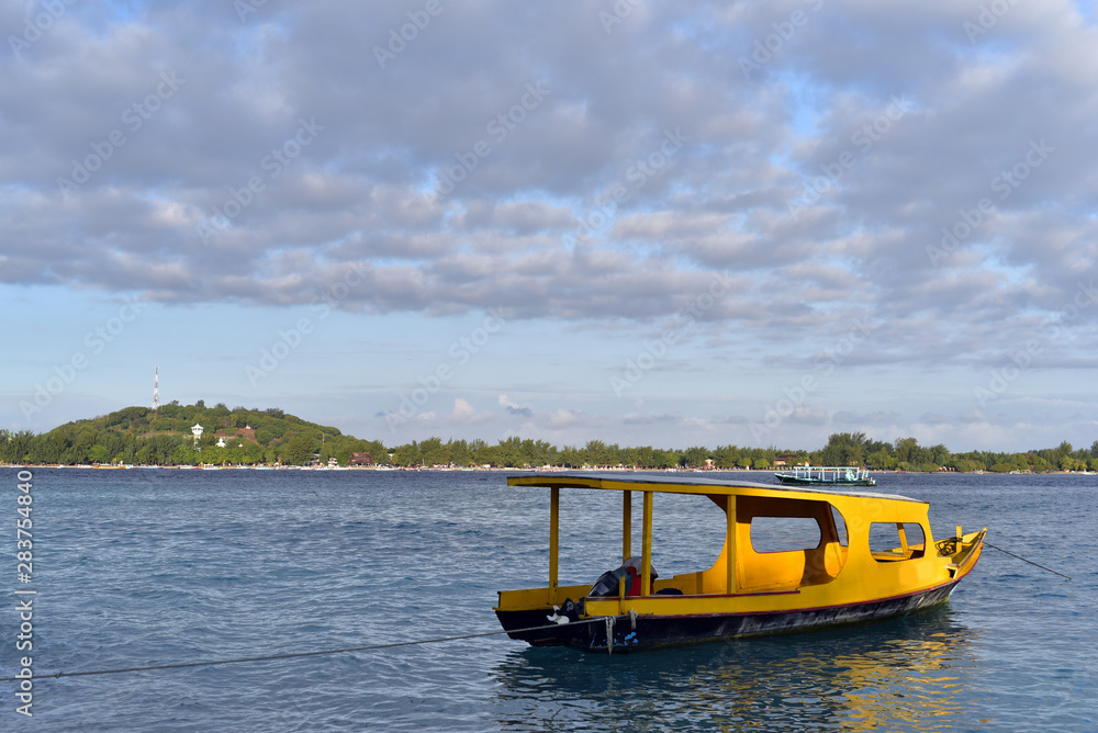 Fototapeta premium Yellow divers boat docked on the shore of Gili Meno Island and Gili Trawangan Island at the background, Indonesia
