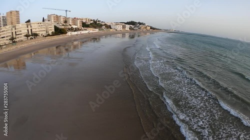 4K. Aerial recording overlooking the horizon, waves breaking against the breakwater, Mediterranean sea, sunset on the beach with a colorful sky, low tide in the port of Santa Maria, Cádiz, Andalusia.