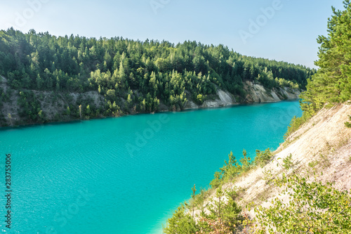 panorama of chalkpit on limestone coast of huge turquoise lake or river near forest. Chalk quarry filled with water