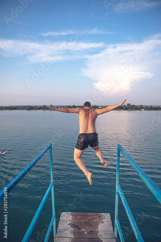 man jumping from tower at lake water on sunset