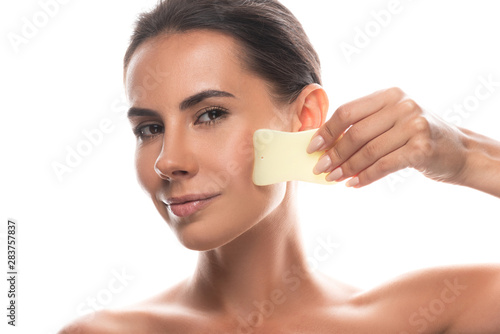 nude smiling young woman using gua sha scraper isolated on white