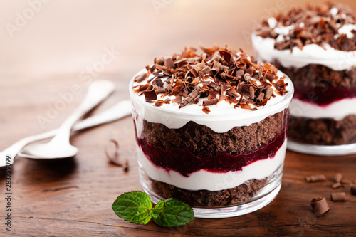 Layered trifle dessert with chocolate sponge cake, whipped cream and fruit jelly in serving glasses. photo