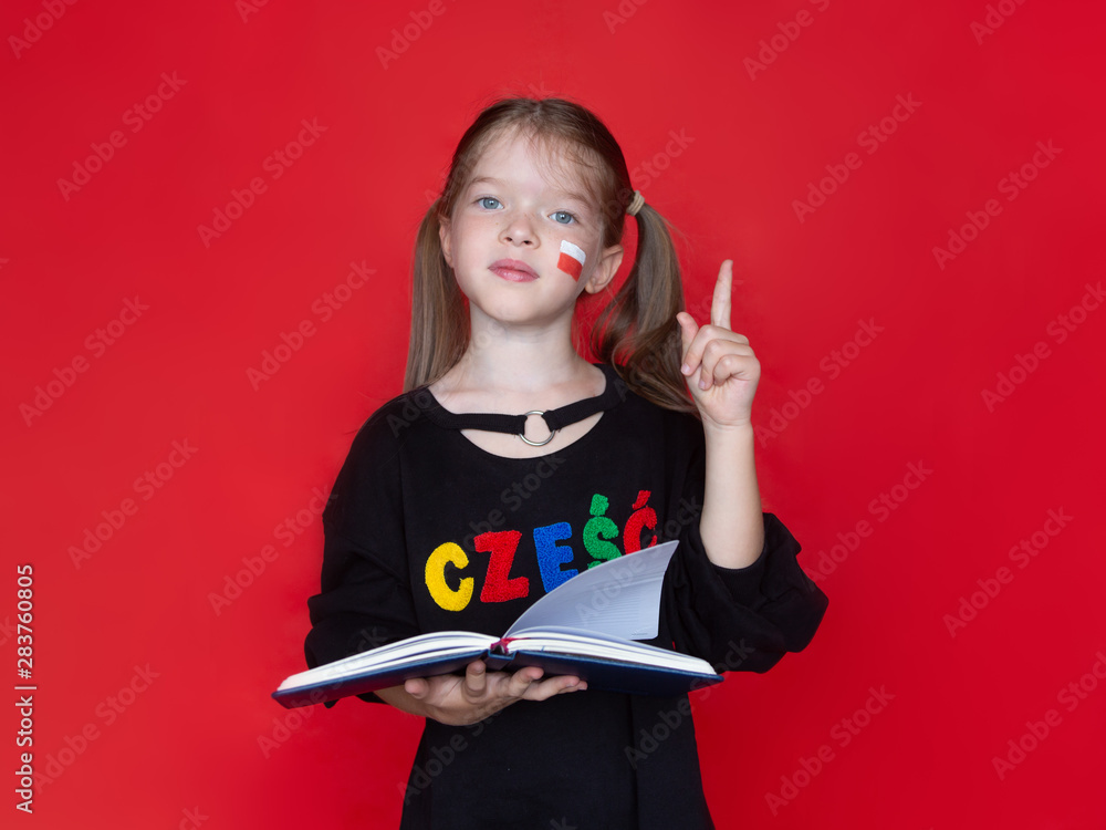 little girl in a black sweatshirt, on her sweatshirt the word Hello in Polish raised her finger up, holds a notebook or book in her hand, Advertising concept for learning Polish