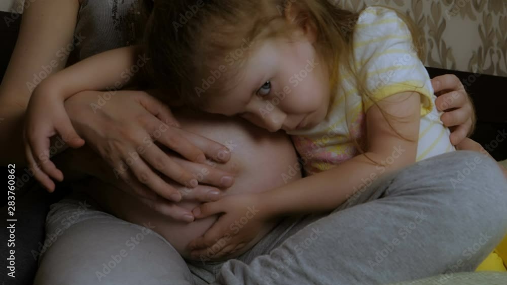 Close-up of a pregnant woman, her husband and daughter hugging her stomach. Close-up of a pregnant woman, her husband and daughter hugging her stomach.