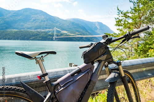 Theme of mountain biking in Scandinavia. human tourist in helmet and sportswear on bicycle in Norway on Hardanger Bridge suspension bridge thrown across the Hardanger Fjord in southwestern Norway photo