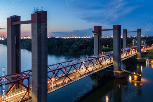 Aerial view of the Spijkenisse bridge over the river Maas at night. Illuminated traffic lane. Blue sky with sunset colors. Industrial lights of the Botlek and the city Hoogvliet in the distance. 