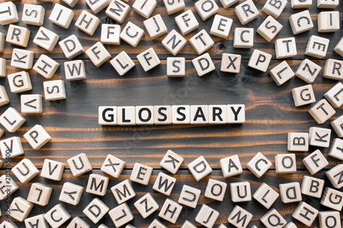 Glossary - word from wooden blocks with letters, alphabetical list with words meanings dictionary glossary  concept, random letters around, top view on wooden background