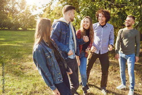 Young people laugh while standing in a park in spring.