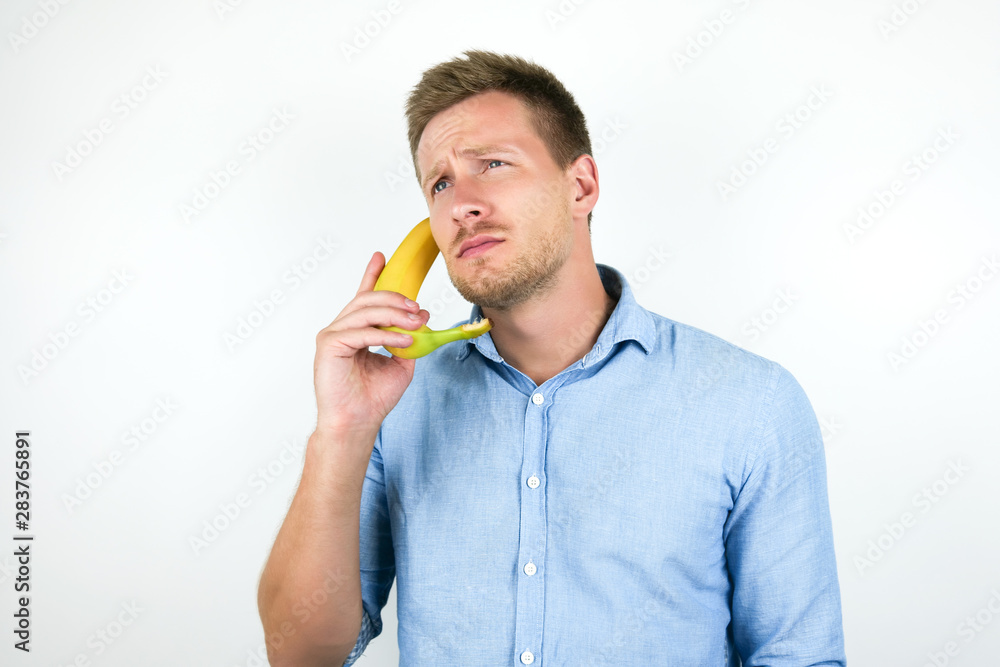 young handsome man holding one fresh banana as a phone near his ear on isolated white background young handsome man holding one fresh banana as a phone near his ear on isolated white background