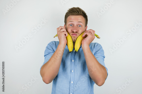 young handsome man holding two fresh bananas near his face on isolated white background