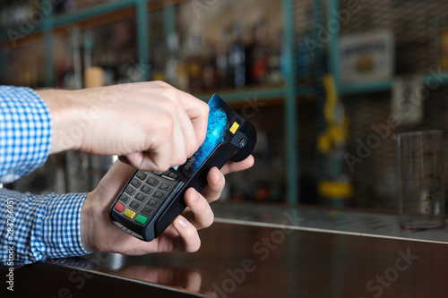 Man using credit card machine for non cash payment in cafe, closeup. Space for text