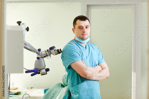 A male dentist is standing with a microscope