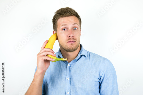 Schilderij op canvas young handsome man holding one fresh banana as a phone near his ear looks suspic