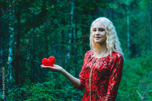 a blonde in a red dress in the woods with a red heart of thread in her handsa blonde in a red dress in the woods with a red heart of thread in her hands photo