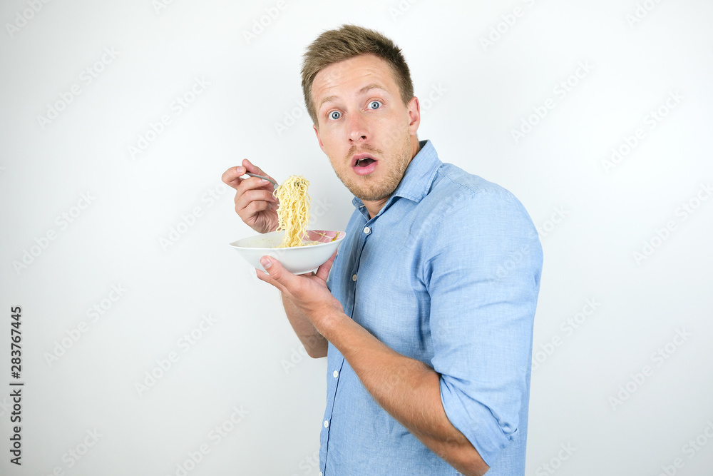 young handsome man eating hot noodles on the go looking hungry on isolated white background young handsome man eating hot noodles on the go looking hungry on isolated white background