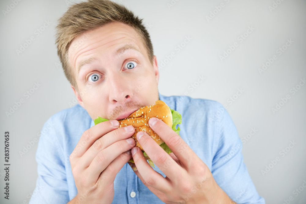 young handsome man biting burger from fast food restaurant looks hungry on isolated white background young handsome man biting burger from fast food restaurant looks hungry on isolated white background