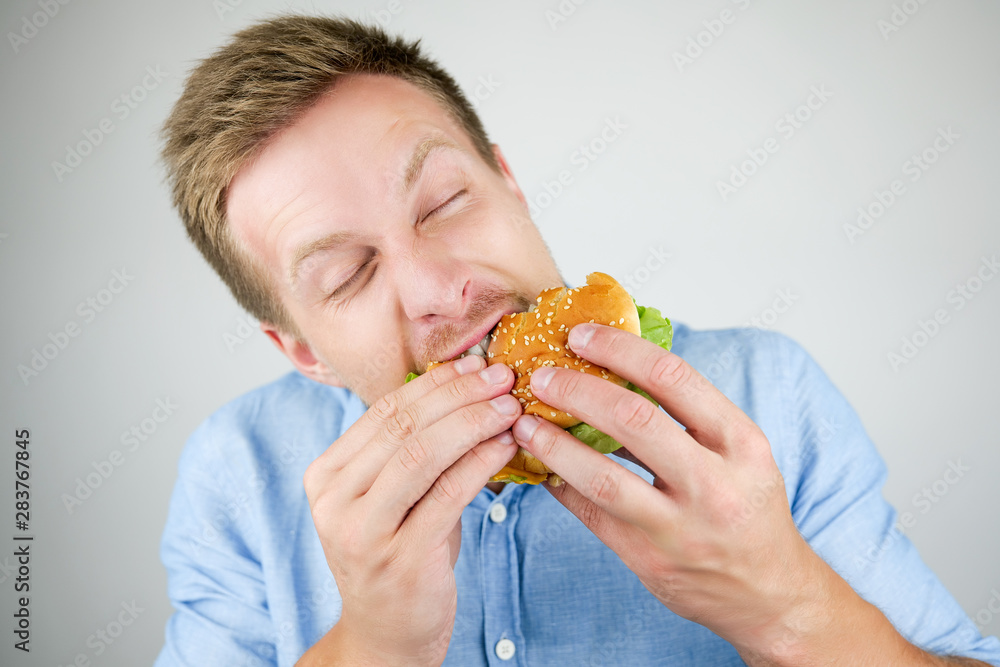 young handsome man biting fresh tasty burger from fast food restaurant looks hungry eating on isolated white background young handsome man biting fresh tasty burger from fast food restaurant looks hungry eating on isolated white background