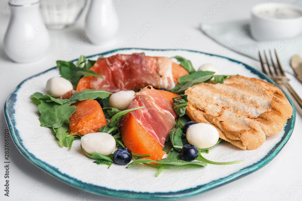 Fresh melon with prosciutto, mozzarella and arugula on white table Fresh melon with prosciutto, mozzarella and arugula on white table