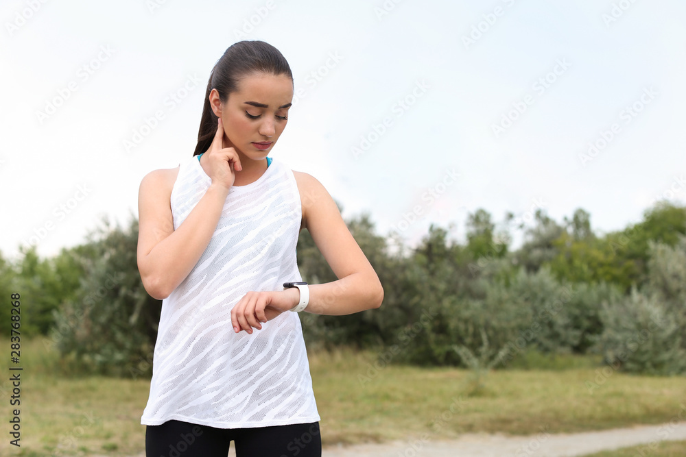 Young woman checking pulse after training in park. Space for text Young woman checking pulse after training in park. Space for text