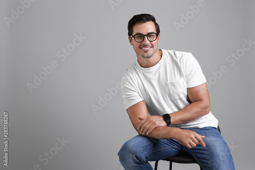 Handsome young man sitting on stool against grey background. Space for text © New Africa