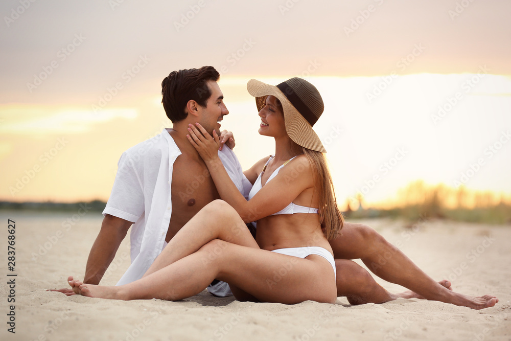 Happy young couple relaxing together on sea beach at sunset Happy young couple relaxing together on sea beach at sunset