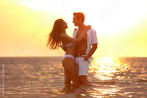 Happy young couple spending time together on sea beach at sunset