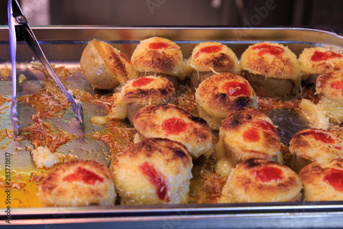 Potatoes covered with cheese gratin on a tray with tongs in the Boqueria market
