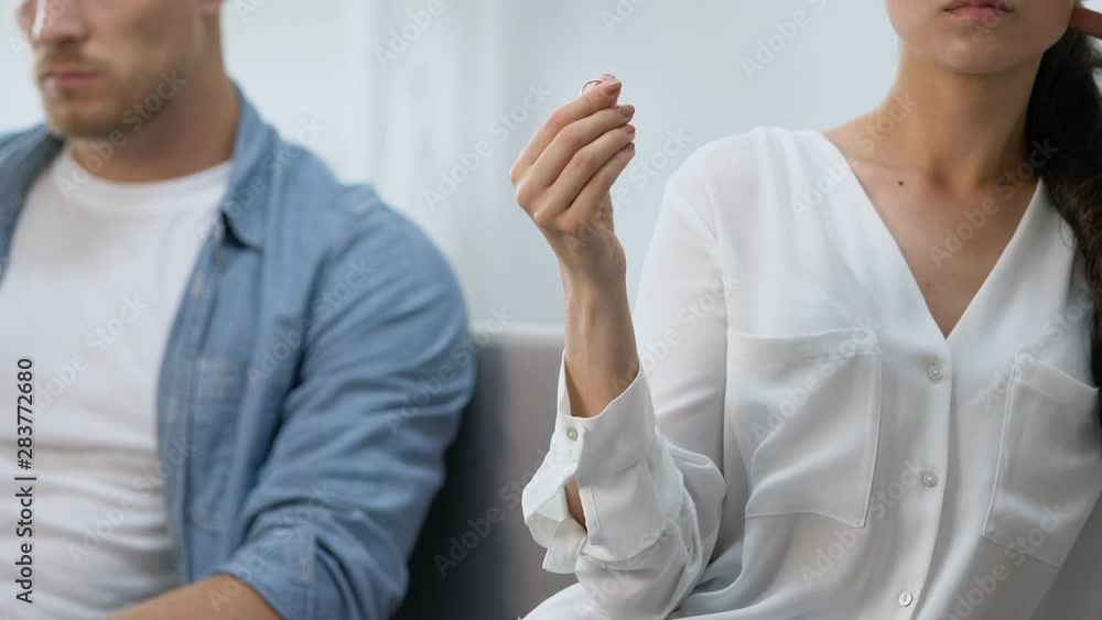 Unhappy wife holding engagement ring in hand, upset husband nearby, divorce risk Unhappy wife holding engagement ring in hand, upset husband nearby, divorce risk