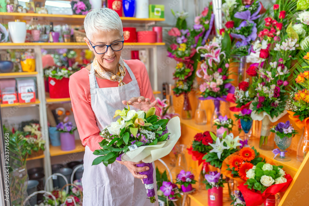 Mature women business owner florist making bouquet in front of flower shop. Cheerful charming mature woman florist standing and holding bouquet in flower shop. Small business.