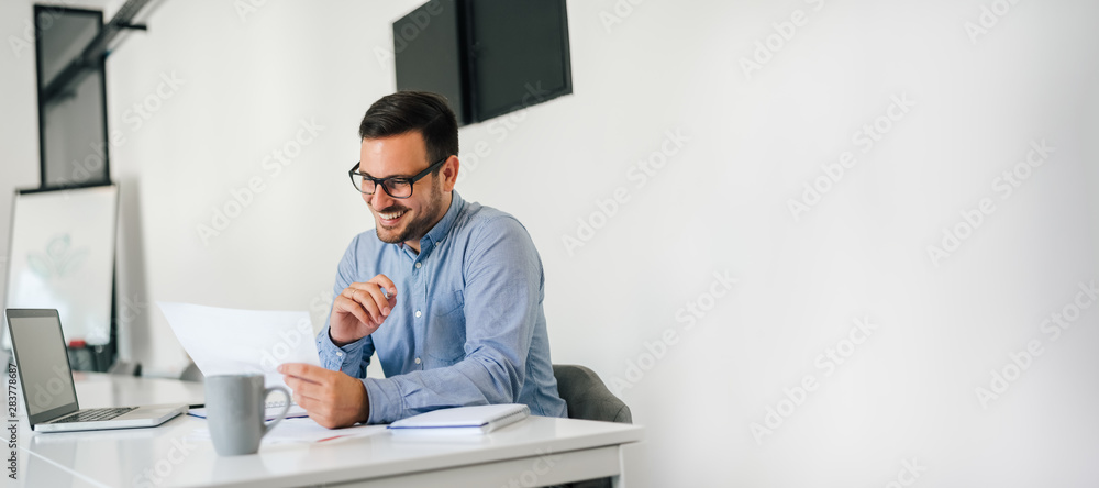 © Moon Safari - Young smiling cheerful confident businessman checking working plan and schedule or timetable in office copy space © Moon Safari - Young smiling cheerful confident businessman checking working plan and schedule or timetable in office copy space