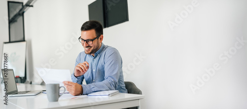 Young smiling cheerful confident businessman checking working plan and schedule or timetable in office copy space photo
