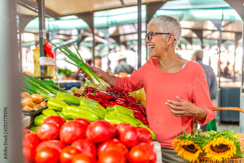 Senior woman on the market. Mature Female Customer Shopping At Farmers Market Stall. Woman shopping at the local Farmers market. Beautiful senior woman buying vegetables.