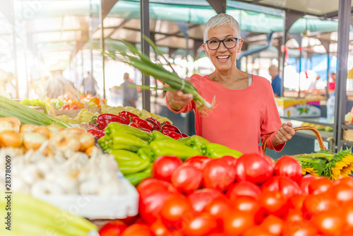 Senior woman buying vegetables at farmers market. Woman picking fresh produce at the market. Senior Woman shopping at an outdoor market. Woman shopping on the farmer's market