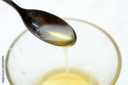 Liquid honey is poured from a teaspoon into a transparent cup. Concept - Healthy Eating