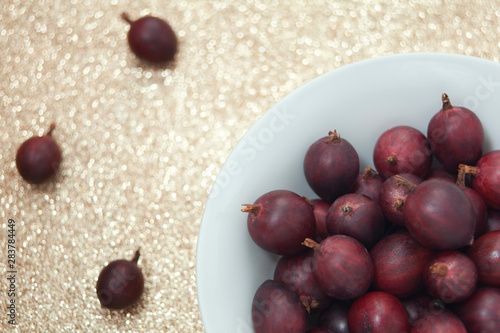Detail shot of red gooseberries in a bowl on a glittering golden background. Photo was taken from above. 