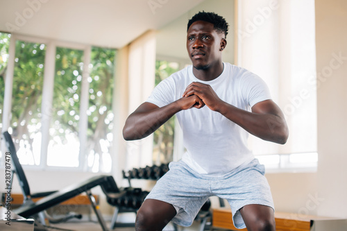 фотографія Concentrated fit African American man in sportswear warming up and doing squat exercise during workout