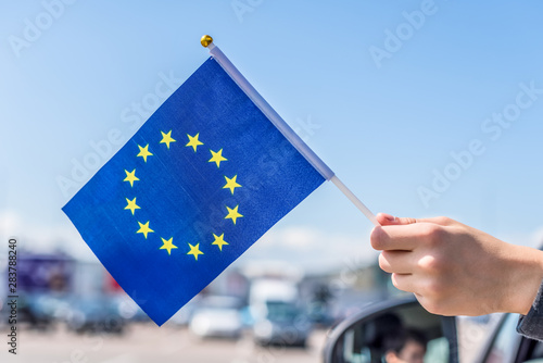 Boy holding Europe or European(EU) Flag from the open car window on the parking of the shopping mall. Concept