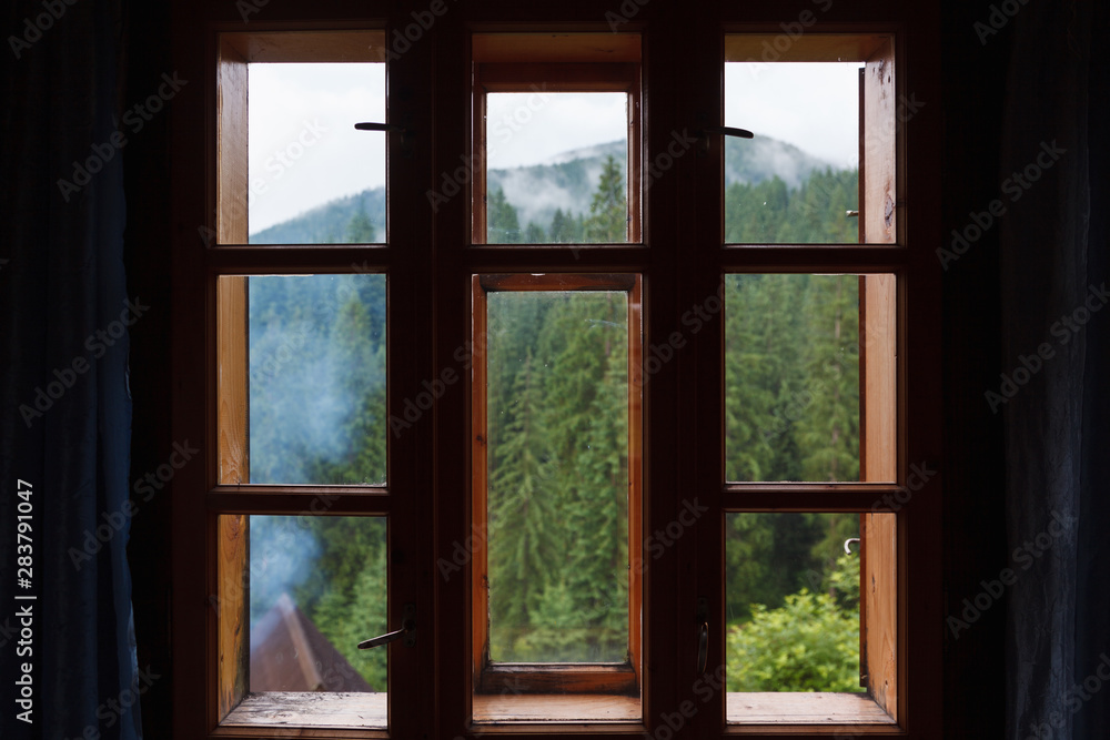 Wooden window behind which a mountain forest is visible. Wooden window behind which a mountain forest is visible.