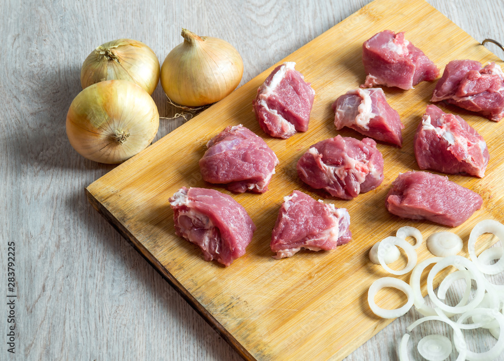 Pieces of raw beef and onion on cutting board
