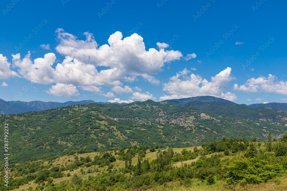 Typical greek summer landscape. Small village on the green hillside with clouds on blue sky. Greece.