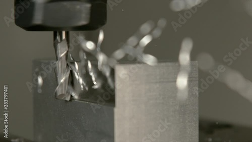 SLOW MOTION, MACRO, DOF: Chips of excess metal come flying off a workpiece during end milling process. Fine cutting end mill drill cuts into the side of a block of metal and creates a mirror finish. photo