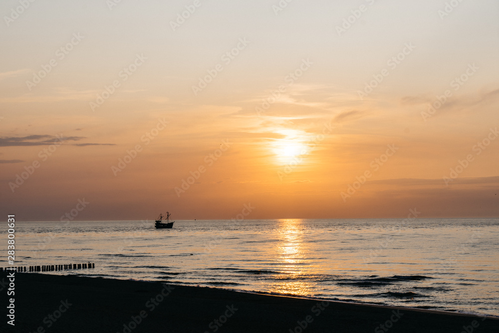 Sunset over the sea horizon in Dziwnow, Poland. Silhouettes of breakwater and ship. 