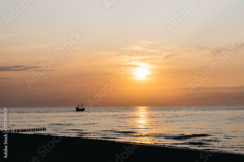 Sunset over the sea horizon in Dziwnow, Poland. Silhouettes of breakwater and ship.  © marcinjozwiak