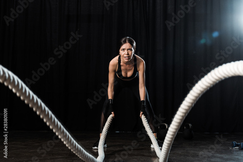 selective focus of woman exercising with battle ropes on black